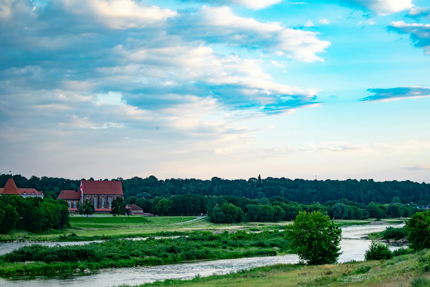 Een kronkelende rivier stroomt langs groene bossen en stenen gebouwen.