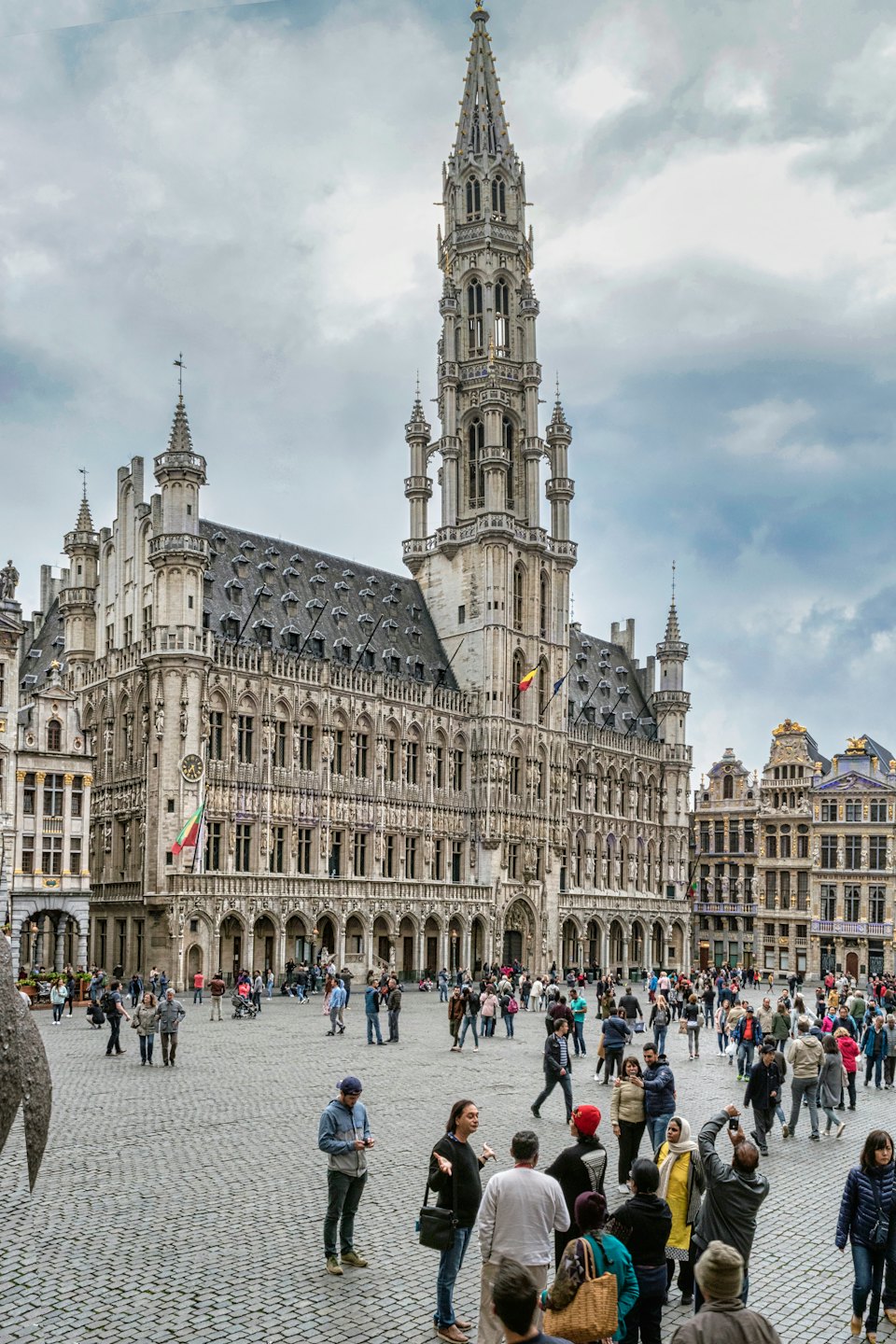 Gotisch stadhuis met spits torent boven druk stenen plein uit.